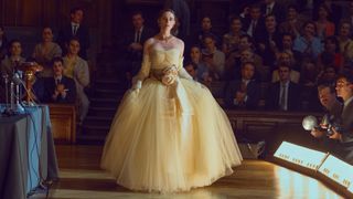 A woman models an off-white dress as dozens of spectators and photographers watch on in The New Look