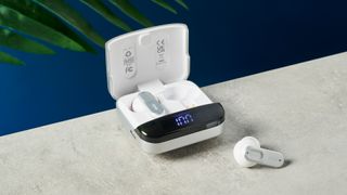 mixx streambuds ultra mini case rests upon a table, with one earbud inside the case and one earbud on the table nearby