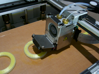 The printer in action. The larger tube at the right feeds plastic filament while the smaller feeds carbon fiber.