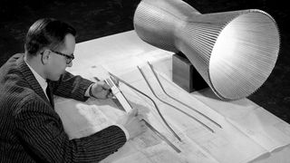 A person sits down at a table with a large drawing of plans to a rocket engine.