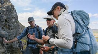 three people stand next to a large boulder, examining it