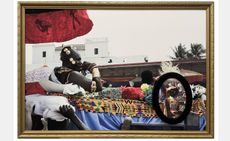 Todd Gray artwork. In a large rectangular gold frame, an African man with a concerned expression wearing gold jewelry reclines, being carried on a platform by other people. A small ovular black frame sits to the right, depicting an old painting of a Black boy with a white hand on his head, gazing up.