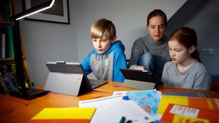 Kids watch on tablets with their older relative behind them.