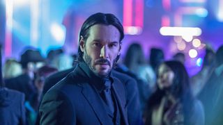 Keanu Reeves as John Wick, standing in a crowd of people with neon in the background in John Wick: Chapter 2