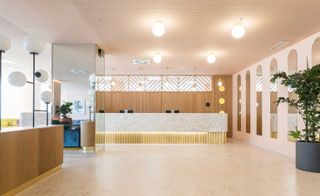 A hotel lobby with a white marble reception counter, a mirrored square pillar, arched wall mirrors, a potted plant and round pendant lights.