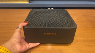 Marantz Model M1 black with hand propping it up on wooden shelf