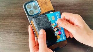 Someone putting a bank card into the back of a MagSafe wallet while holding an iPhone.