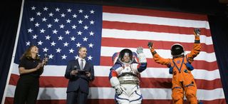 Amy Ross, a spacesuit engineer at NASA’s Johnson Space Center, left, and NASA Administrator Jim Bridenstine, second from left, watch as Kristine Davis, a spacesuit engineer at NASA’s Johnson Space Center, wearing a ground prototype of NASA’s new Exploration Extravehicular Mobility Unit (xEMU), and Dustin Gohmert, Orion Crew Survival Systems Project Manager at NASA’s Johnson Space Center, wearing the Orion Crew Survival System suit, right, wave after being introduced by the administrator, Tuesday, Oct. 15, 2019 at NASA Headquarters in Washington.