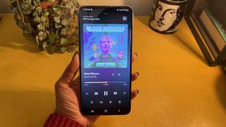 The Samsung Galaxy S22 Plus held in front of a yellow surface. On screen is 'Heat Waves' by Glass Animals on Tidal.
