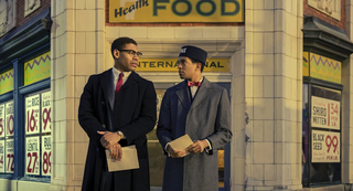 Aaron Pierre star of Genius: MLK/X, wearing a smart suit and red tie, stands in front of a vintage American building 