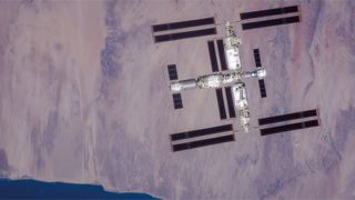 a large T-shaped space station is seen from above with Earth below it