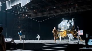 people in white spacesuits walk across a movie set built to resemble the surface of the moon