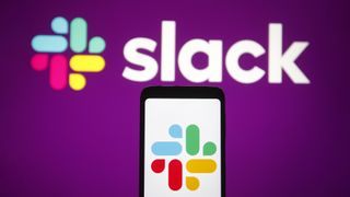 The slack logo on a mobile phone in front of a purple wall with the slack logo on it