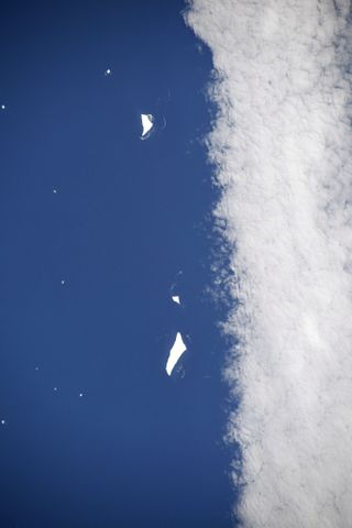 a sea of blue divided on the right by a column of cloud. in the water a few icebergs float like small white fragments