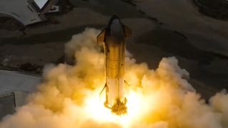 fire, dust and exhaust billow from the base of a big, stainless steel rocket