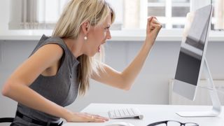 A woman shaking her first angrily at an iMac.