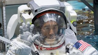 an astronaut in a spacesuit in the harness in the water, waving at the camera 