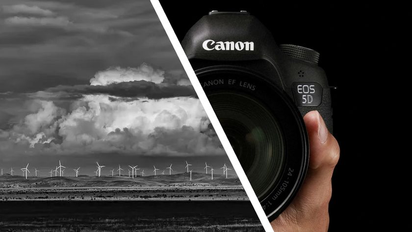 Monochrome image of a distant wind farm alongside a Canon DSLR camera in the hand with black background