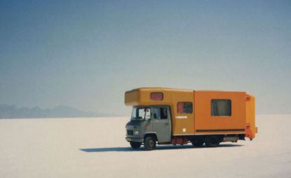 A large caravan with a green front and orange caravan section that extends back through the vehicle. 