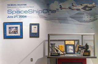 several plaques and other mementos on a white wall beneath the word "spaceshipone"