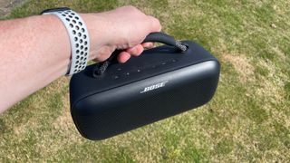 Bose SoundLink Max wireless speaker held in hand above grass