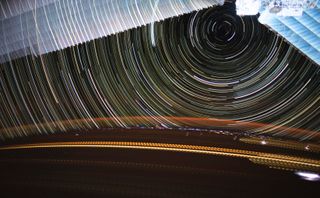 Light trails streak across the Earth as star trails circle overhead in this stunning long-exposure photo taken by NASA astronaut Christina Koch at the International Space Station. At the top of the frame are the space station's solar arrays. Down below, flashes of lightning are scattered across the Earth's surface, while orange airglow illuminates the atmosphere.