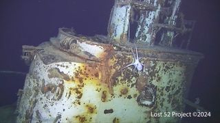 A photo of a rusty submarine underwater with an octopus crawling on it