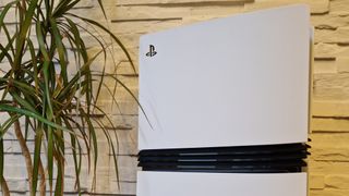 PS5 Pro puisella pöydällä huonekasvin vieressä ja valkoisen seinän edessä