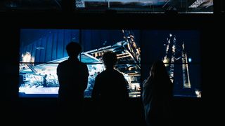 photo showing three silhouetted people in the foreground looking at a projection of a rocket's launch tower