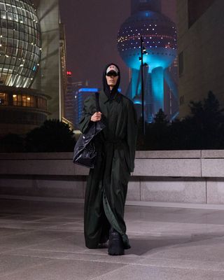 Man on runway in Balenciaga platform boots and long coat with Shanghai skyline as backdrop