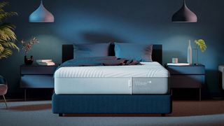 Image shows the Casper Wave Hybrid Snow Mattress in white placed on a deep blue fabric bed frame in a dark blue bedroom