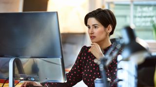 A woman with short dark hair looking seriously at a computer