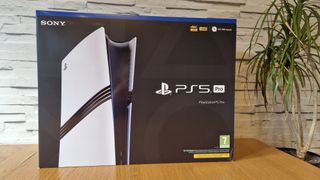 PS5 Pro -myyntipaketti puisella tasolla huonekasvin ja valkoisen koristeseinän vieressä