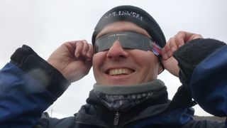 a man wearing eclipse glasses and a hat, he is smiling. 