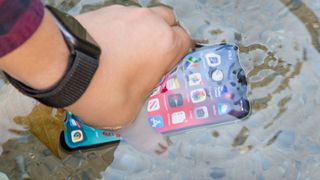 A hand dunking an iPhone in water to test its water resistant capabilities