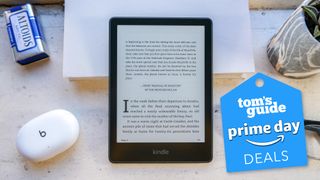 A Kindle Paperwhite on a desk surrounded by items including headphones, glasses and a plant