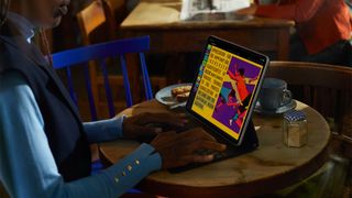 A woman sat at a table, using an iPad propped up on a keyboard