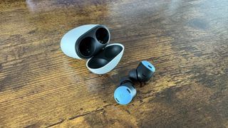 Google Pixel Buds Pro in-ear headphones next to charging case on wooden surface