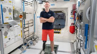 john mcfall standing in an international space station module with a prosthesis visible on one of his legs