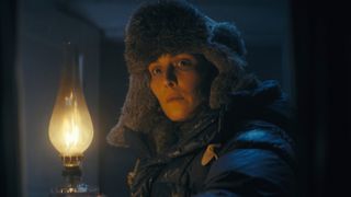 Woman holding a lit lamp. She is wearing a thick winter hat and jacket