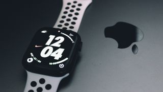 The Apple Watch series 8 with a white strap pictured next to another Apple Device with a shiny Apple logo