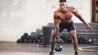 Man lifting a heavy kettlebell using right arm in a half squat position during gym workout