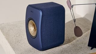 A blue KEF LSX II speaker on a stone surface.