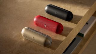 The new Beats Pill in three different colours - gold, red and black - displayed on wooden table