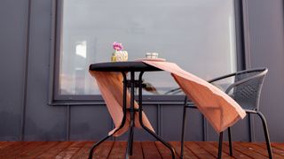 A table and chairs outside a window with the table cloth blowing in the wind