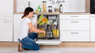 A woman emptying a dishwasher filled with colorful plates