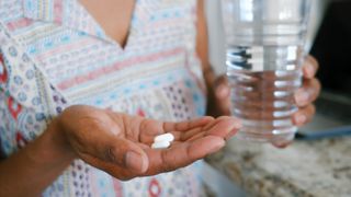 Close-up of a woman's hands, one holding two oblong white tablets, resembling tylenol, and the other holding a glass of water