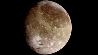 Ganymede imaged by NASA&#039;s Galileo spacecraft appearing as a sandy brown colored cratered moon. with the left portion partly in shadow.