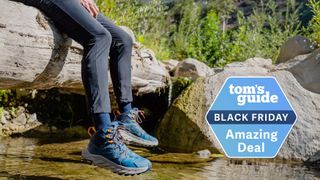 A person wearing Hoka boots next to a stream with grass in the background.