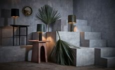 Elegant tableware brand L’Objet presented its new collection ’Tulum’. Different shaped side tables with lamps on concrete steps with palm leaves next to them.